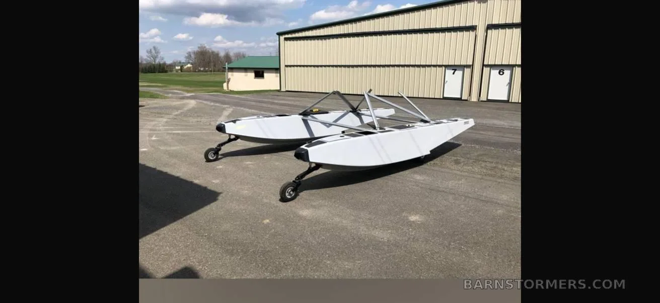 Two white aircraft floats on wheels are parked on asphalt in front of a hangar.