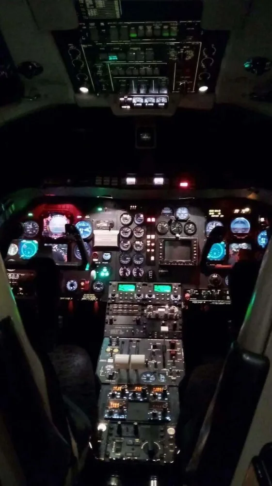 An illuminated aircraft cockpit at night, showing glowing instruments, screens, and control panels.