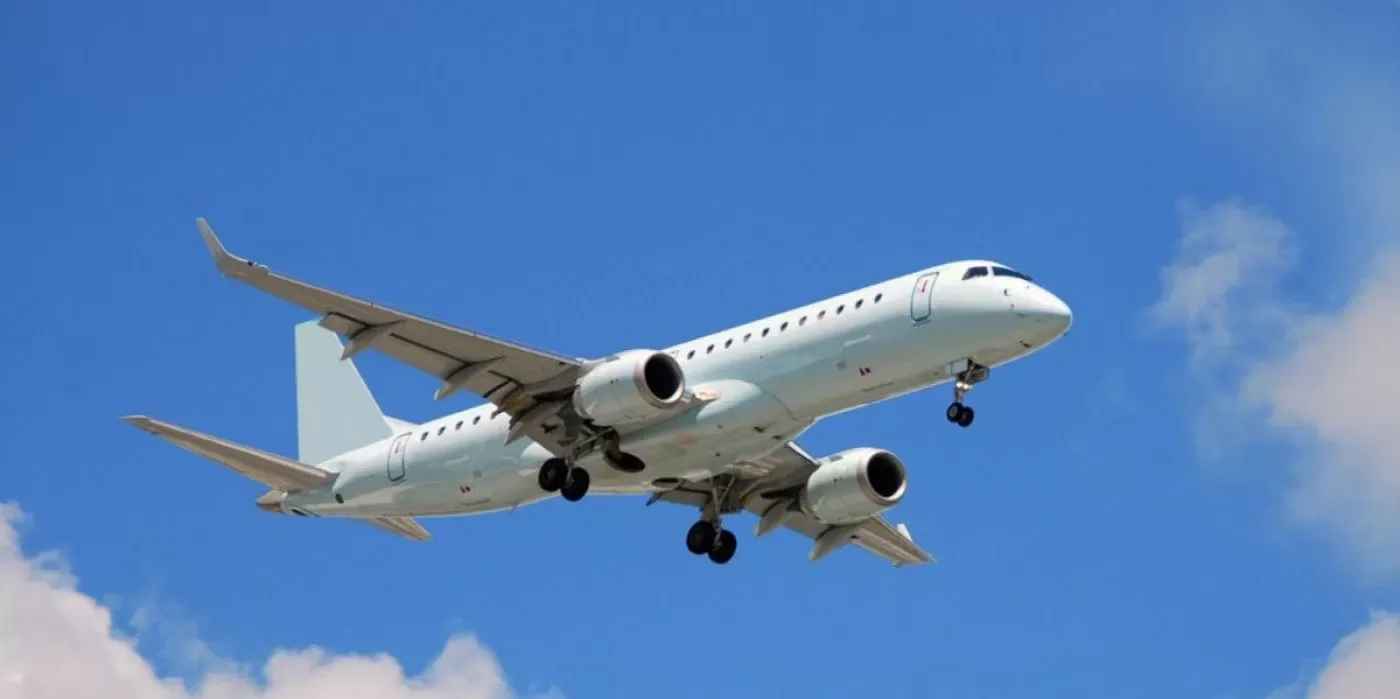 A white twin-engine regional jet with landing gear extended, flying against a clear blue sky.