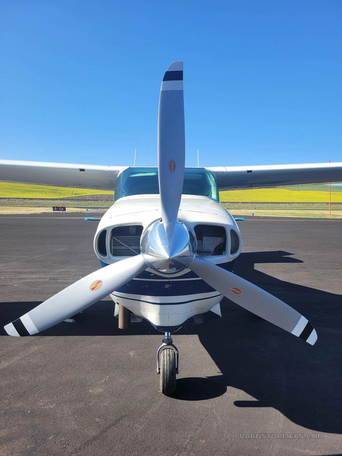 A close-up front view of the propeller and nose of a white and blue Cessna T206H Turbo Stationair.