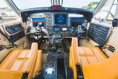 The cockpit of a turboprop aircraft features a modern glass panel display and tan leather seats.