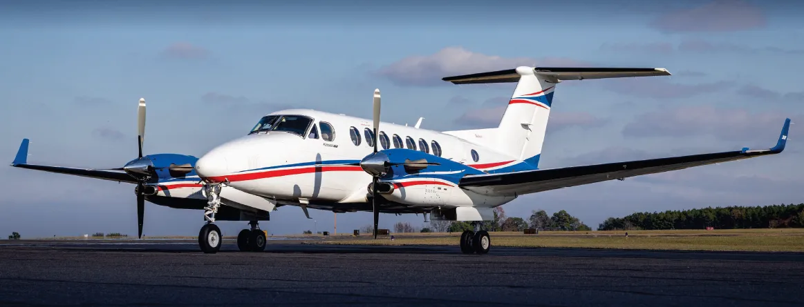 Side view of a white Beechcraft King Air 360 with blue and red stripes parked on a tarmac.