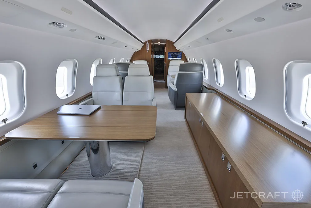 A wide view of the Bombardier Global 6000 cabin, showing a conference area with a large wooden table and a credenza along the wall.