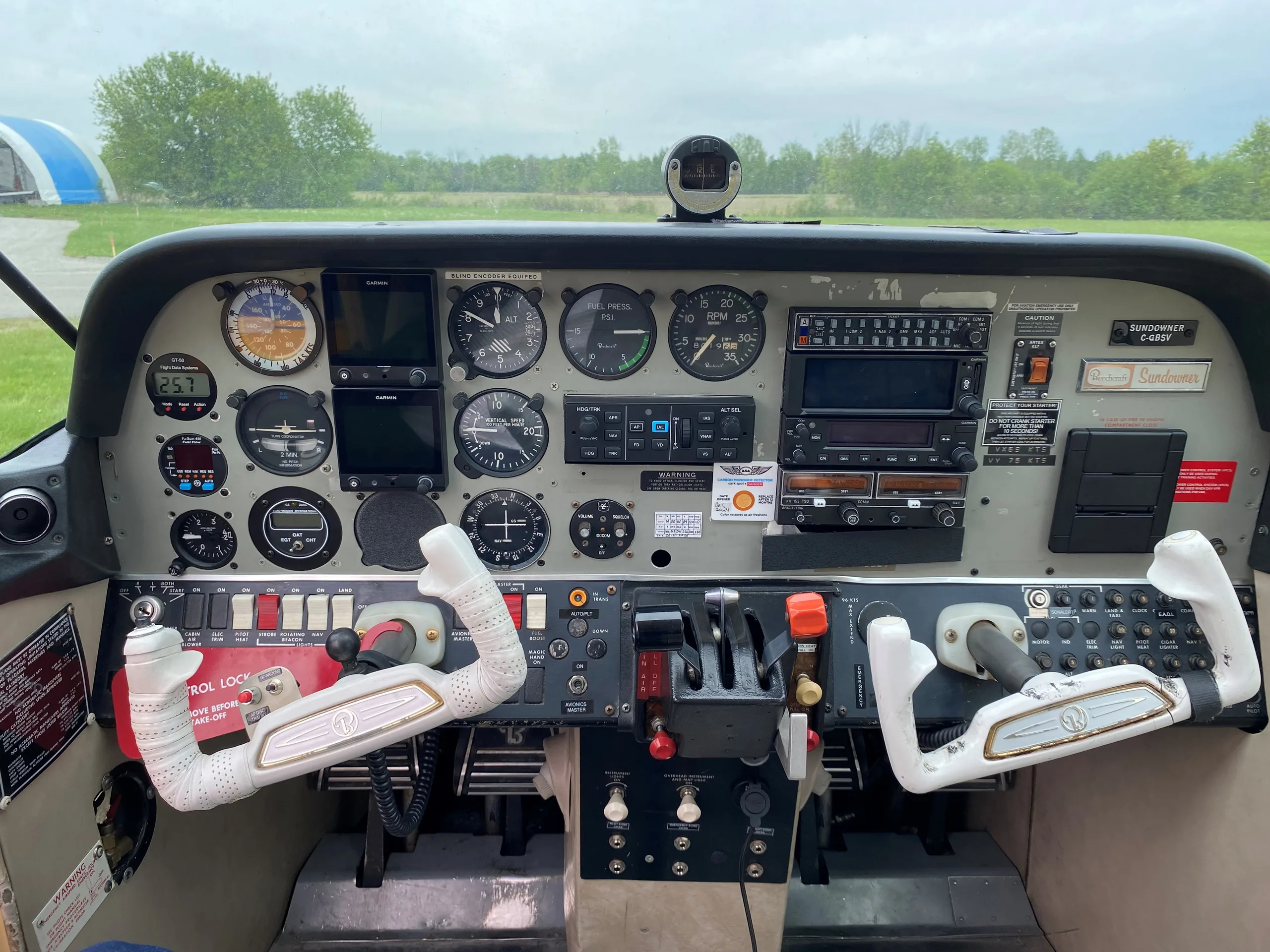 The full instrument panel of a Sundowner C-23 aircraft with dual yokes and a view of the airfield.
