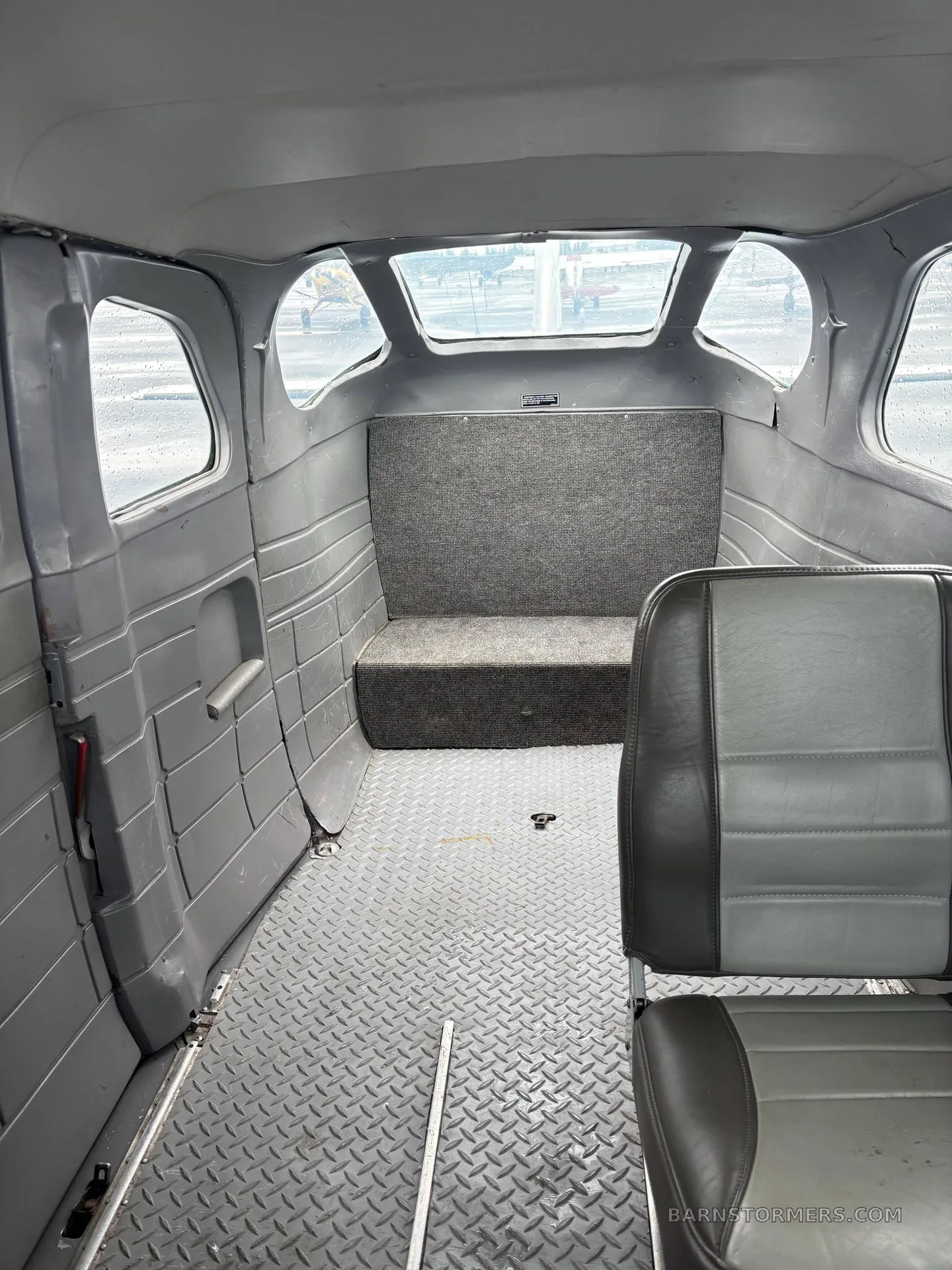 The gray interior cabin of an aircraft, showing a rear bench seat and diamond plate floor.
