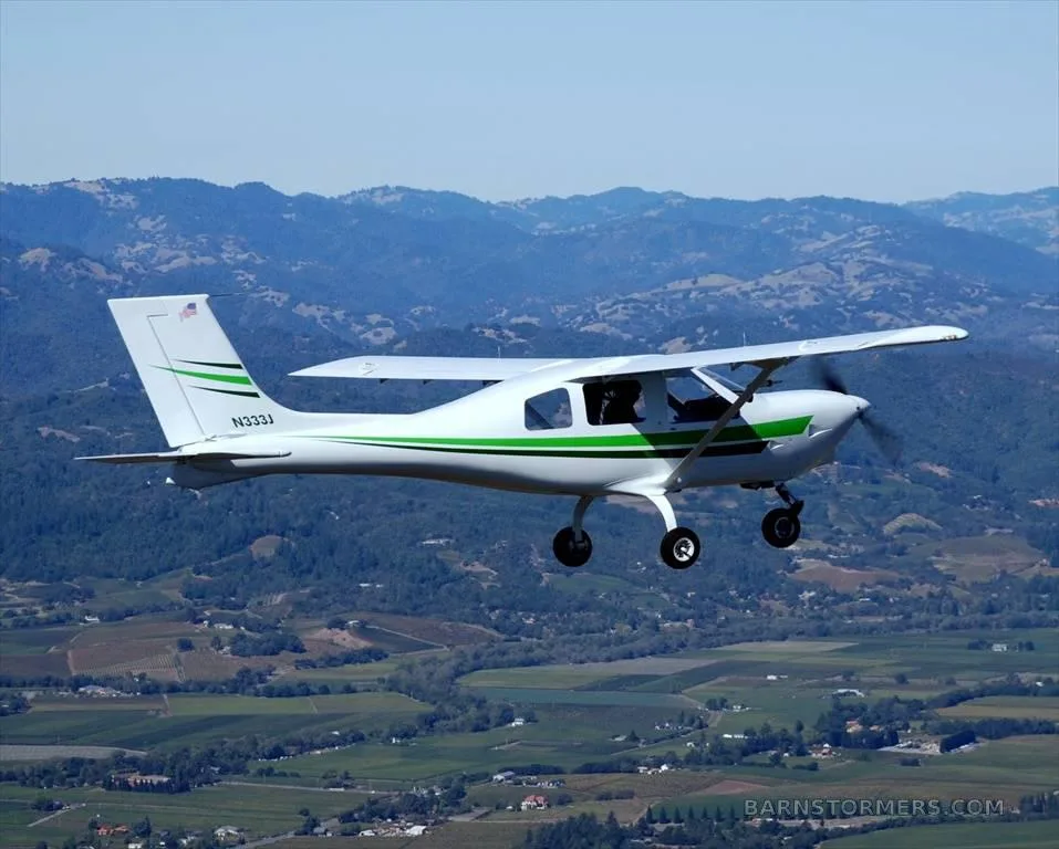 A white and green light aircraft (N333J) flies over a mountainous, green landscape.