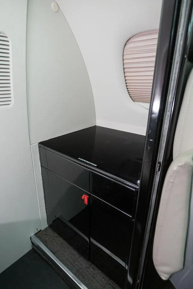 A black glossy storage cabinet with two drawers and a flat top surface inside the cabin of a business jet.