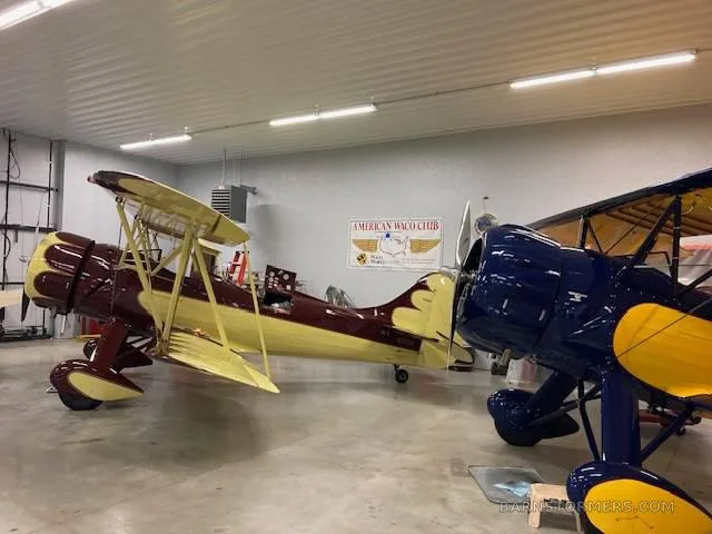 Two vintage biplanes, one maroon and cream, and one blue and yellow, are parked inside a hangar.
