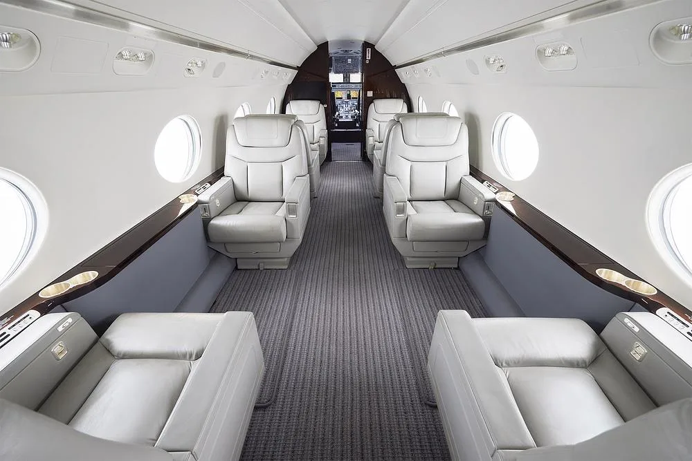 Interior view of a business jet cabin with light grey leather seats and a patterned carpet.