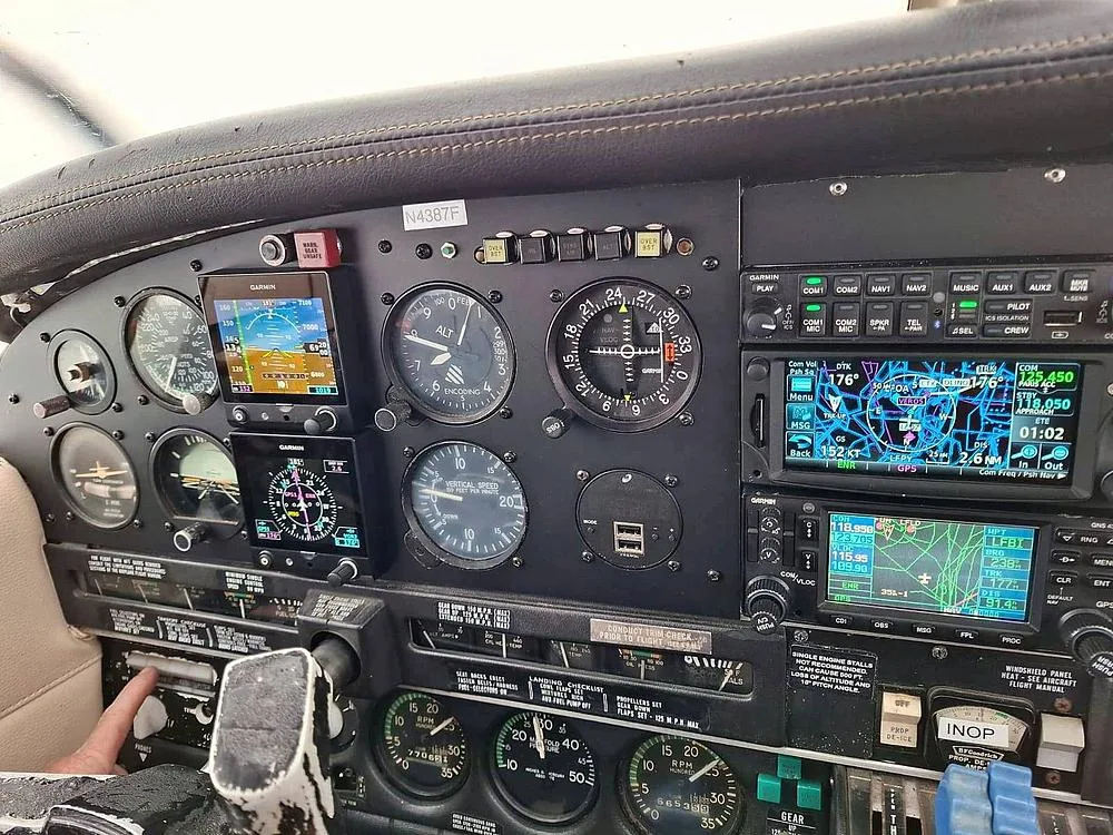 A detailed view of the cockpit instrument panel of the Piper PA-34 Seneca II, N4387F, featuring multiple Garmin displays and analog gauges.