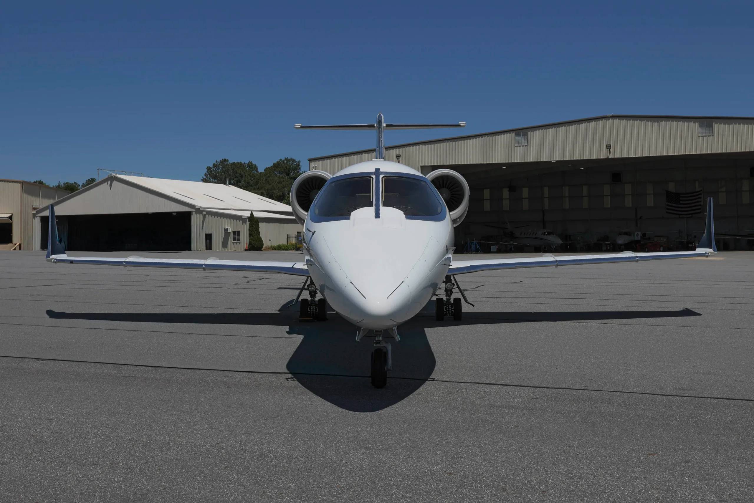 A white business jet with engines mounted on the rear fuselage, viewed head-on on an airport tarmac.