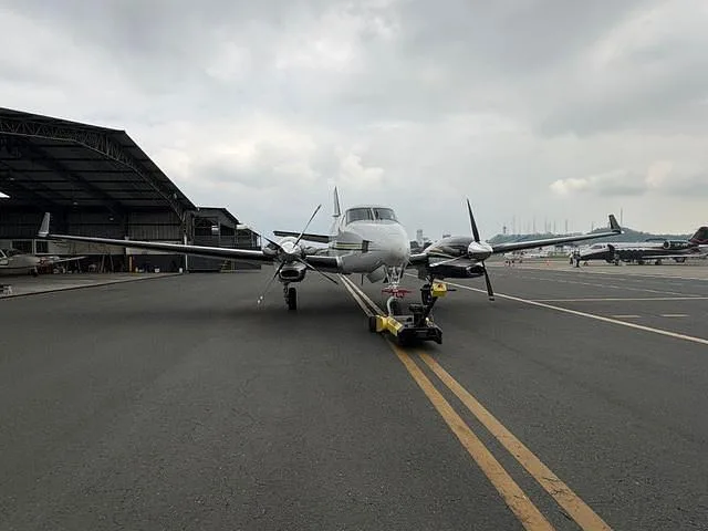 A white and black twin-engine turboprop aircraft being towed on an airfield, viewed from the front.