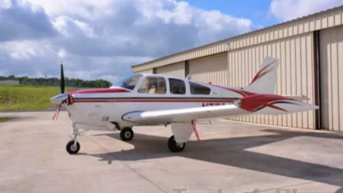 A white and red Beechcraft Bonanza N43731 parked on a tarmac next to a hangar.