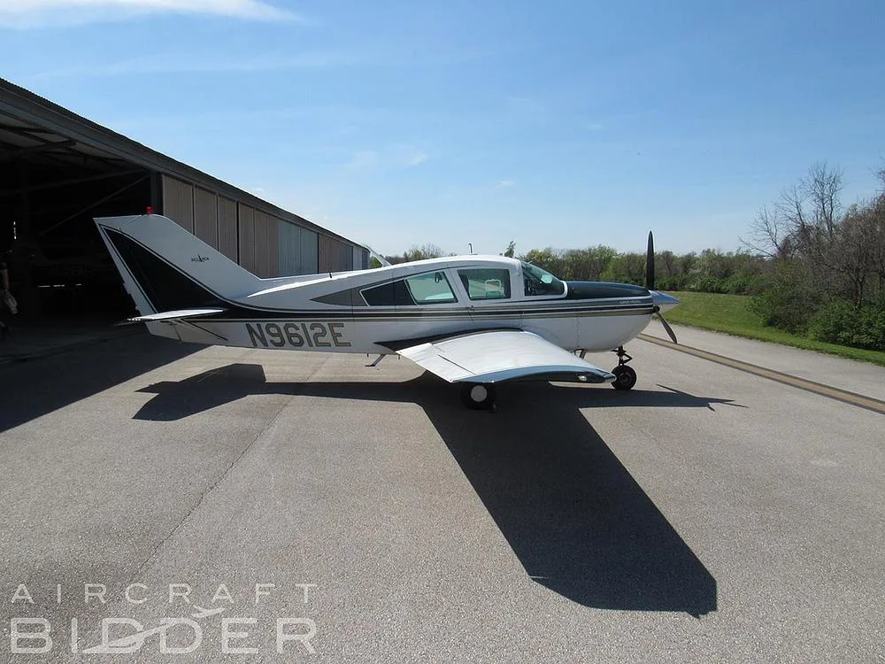 A three-quarter view of the white and dark green single-engine aircraft N9612E parked on a tarmac next to a hangar.