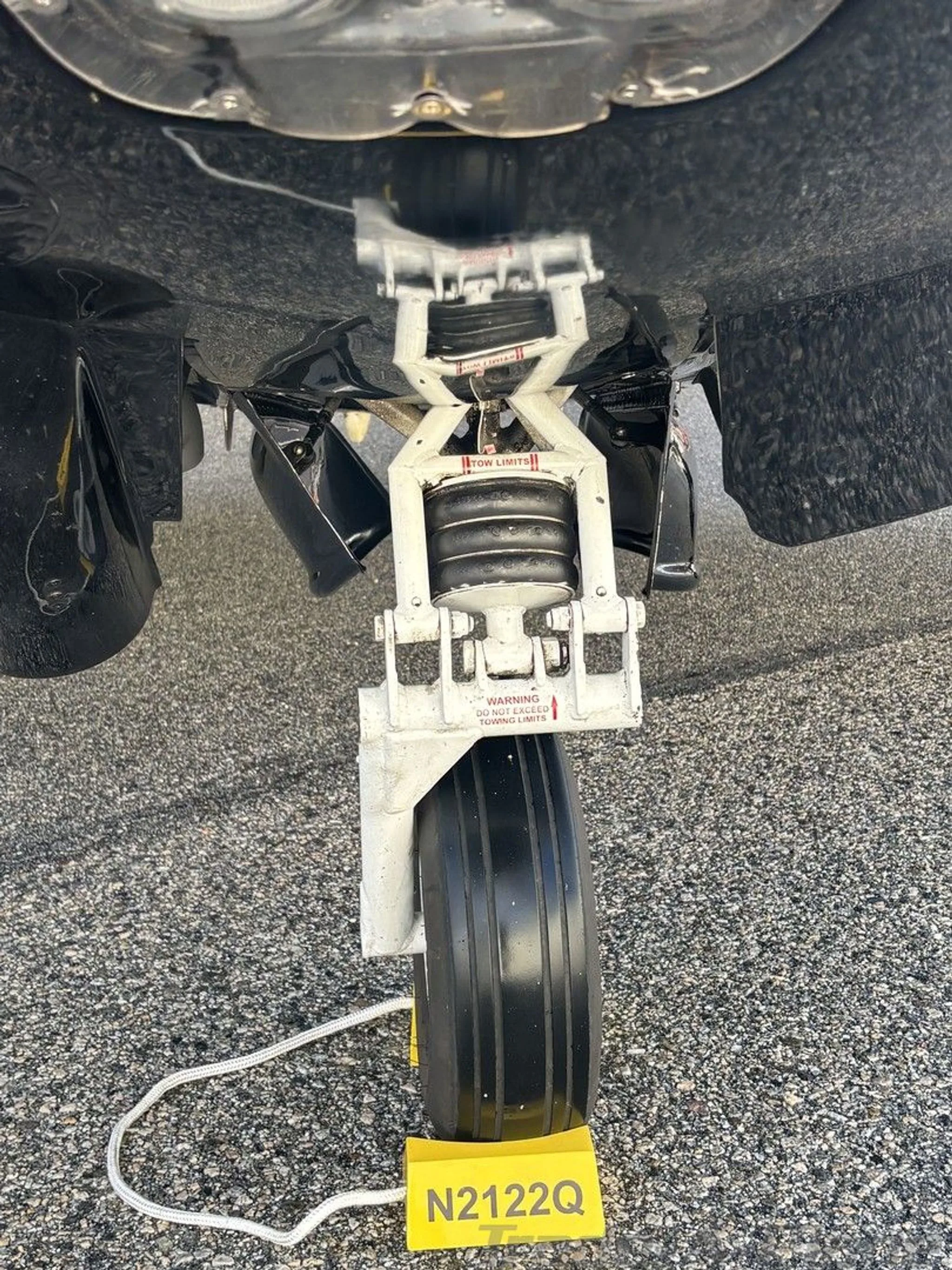 An overhead view of the nose landing gear of a Mooney M20K aircraft, with a yellow chocks displaying N2122Q.