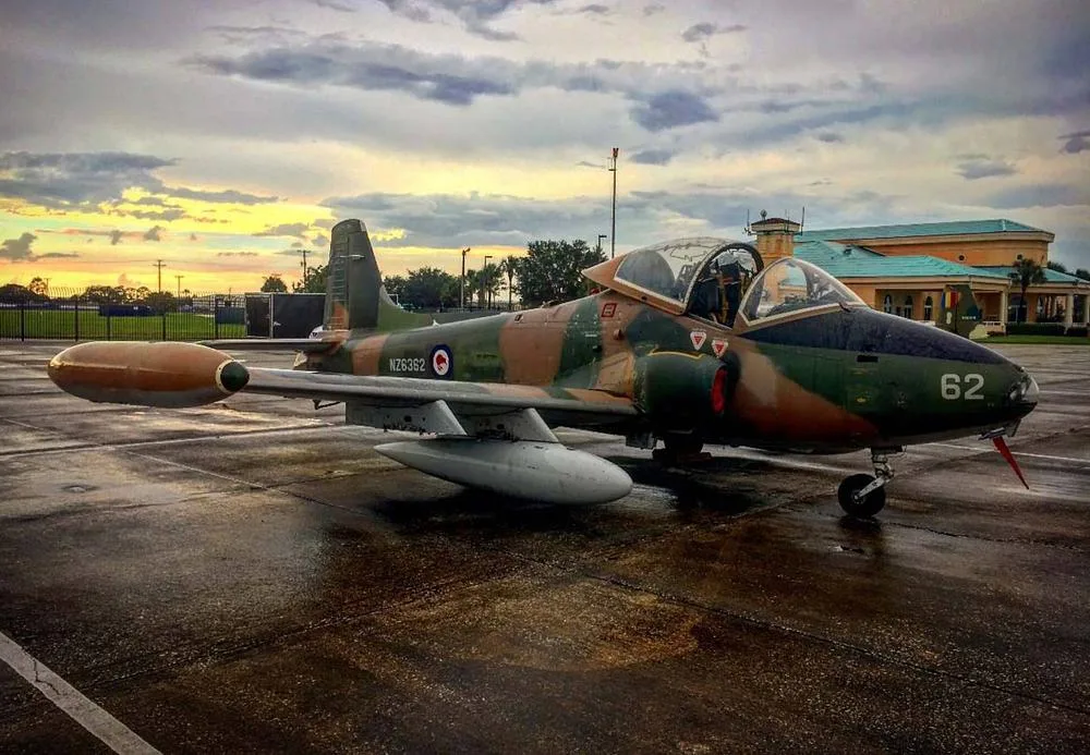 A Royal New Zealand Air Force BAC Strikemaster Mk.88 (NZ6362) in camouflage paint scheme on a wet tarmac at sunset.