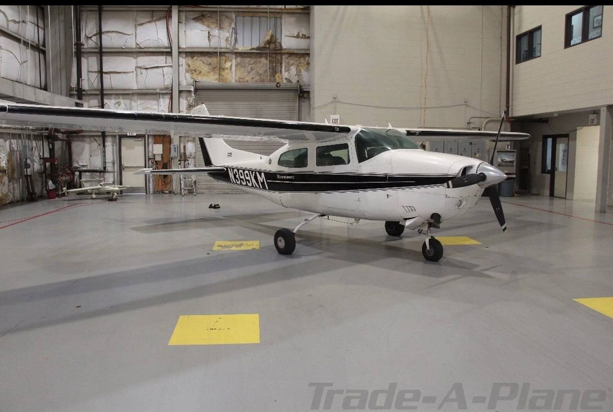 A white Cessna 210 Centurion with black stripes, seen from the front-right in a hangar.
