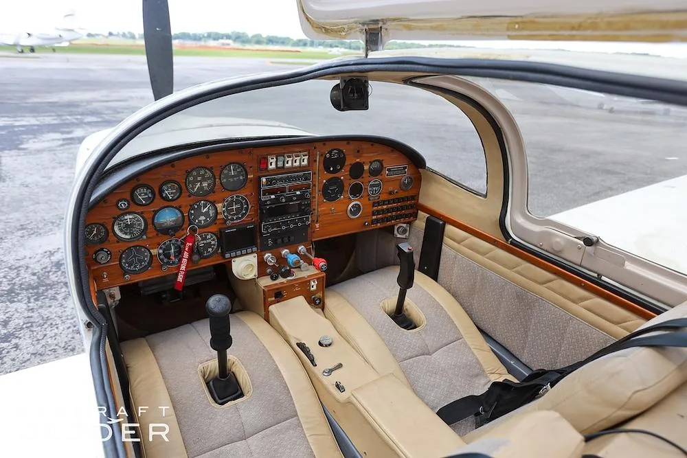 The cockpit of the aircraft with a wooden instrument panel, dual joysticks, and tan and beige seats.