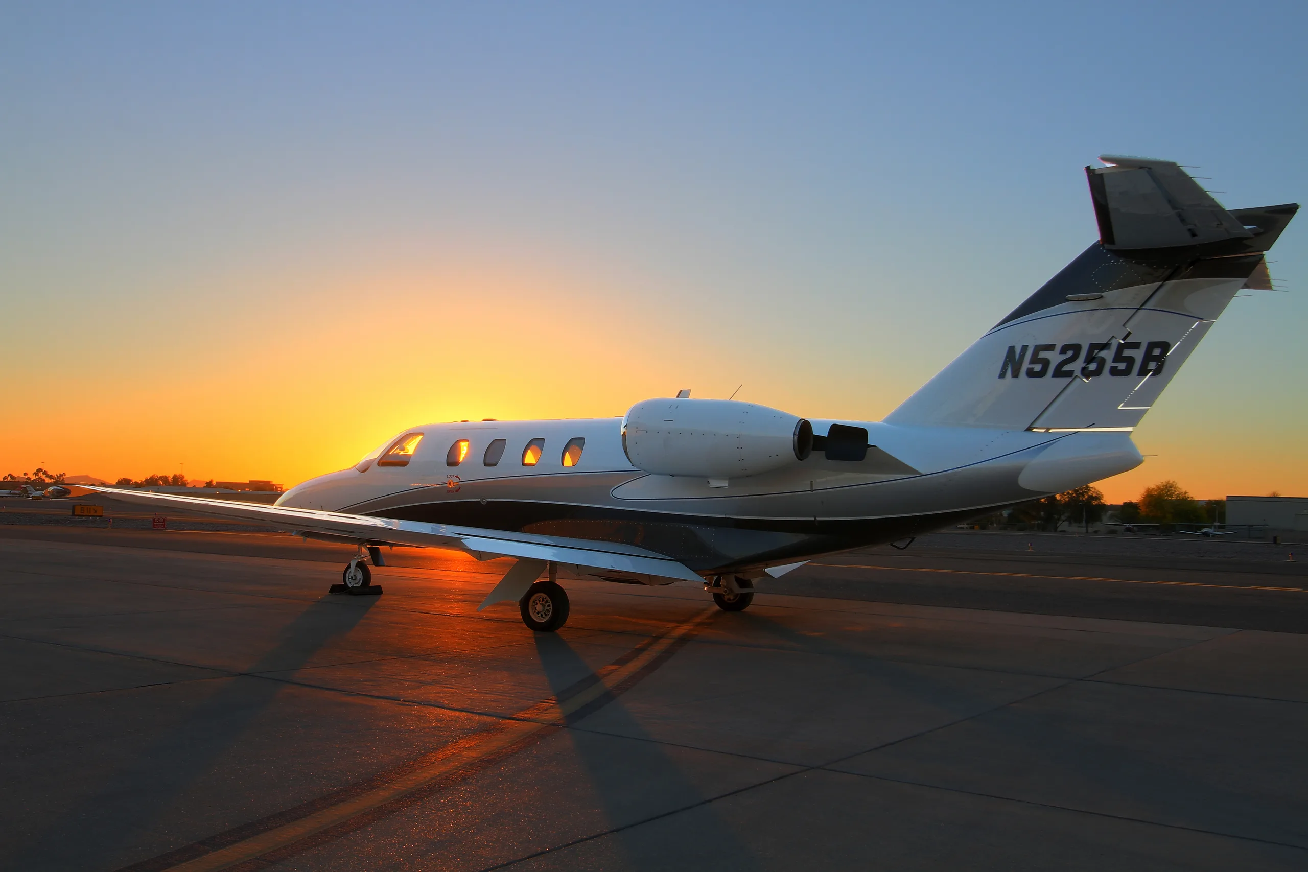 A white and dark grey business jet with registration N5255B is parked on an airport tarmac at sunset.