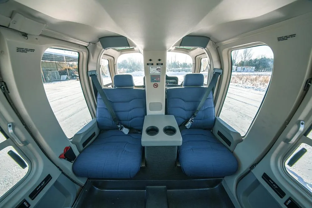 The front passenger cabin of a helicopter with two blue fabric seats and a center console.