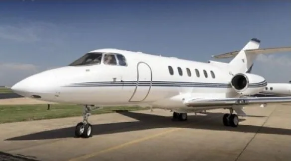 A white business jet with dark stripes on the fuselage, parked on an asphalt tarmac under a clear sky.