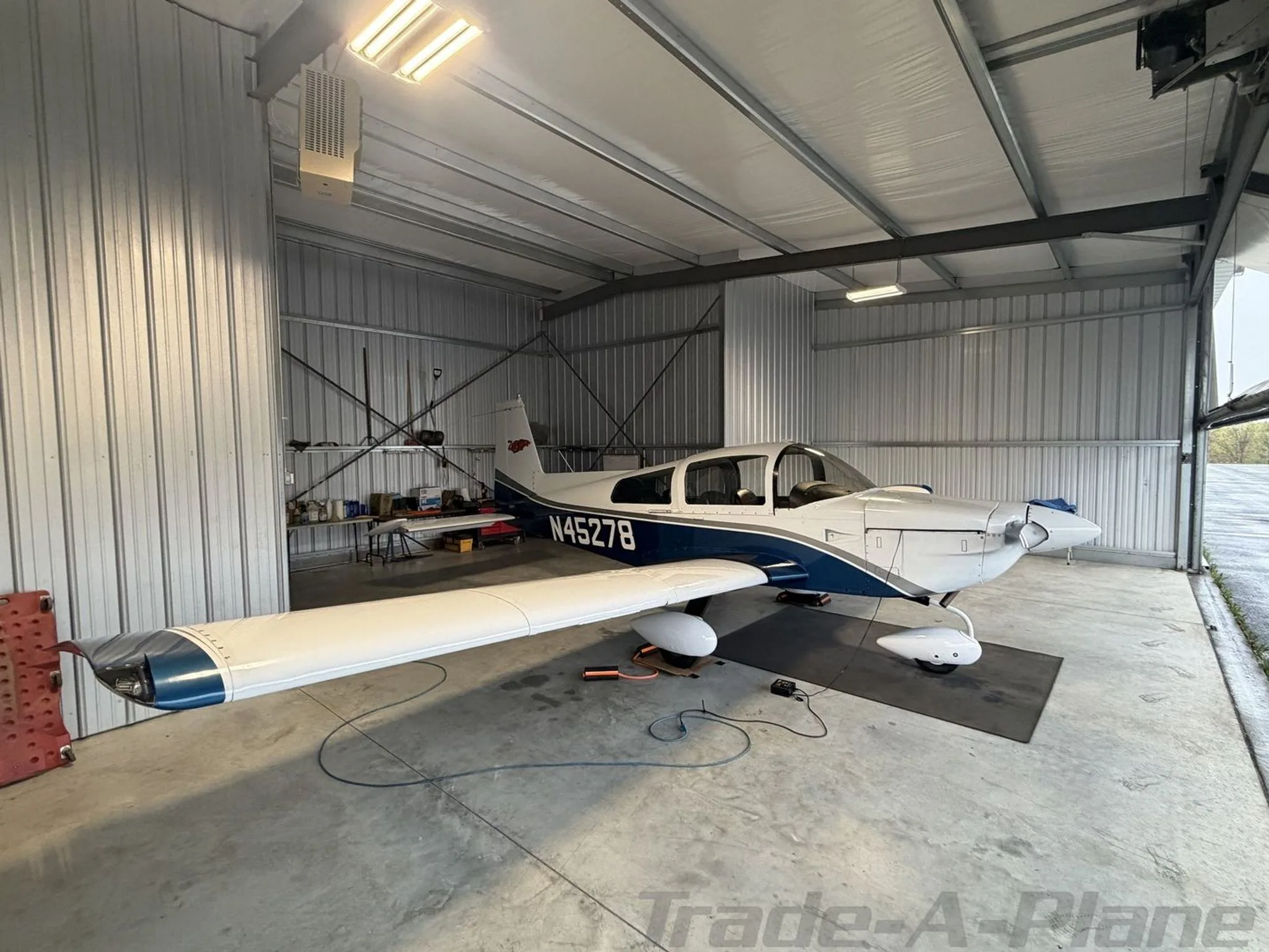Front-right view of a white and blue Grumman AA-5B Tiger N45278 in a hangar.