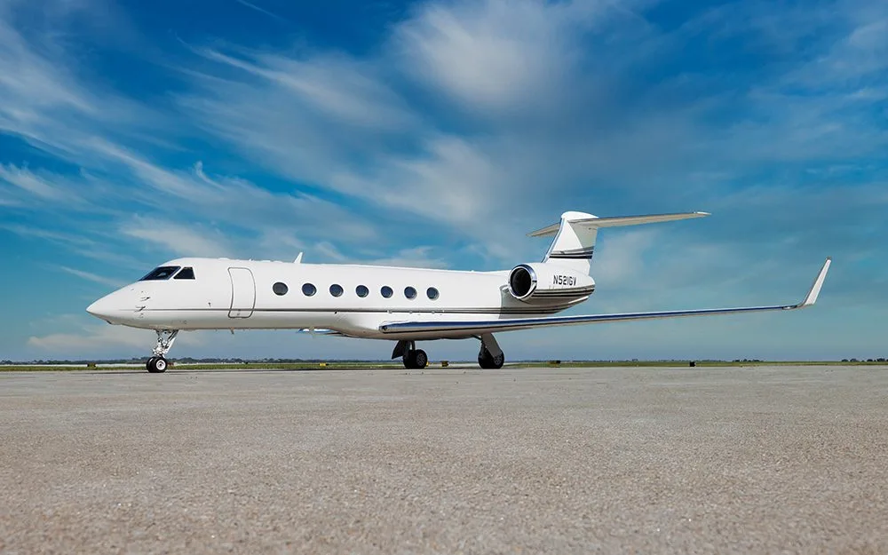 A white Gulfstream G550 business jet with a black stripe on the tail, parked on a tarmac under a blue sky.