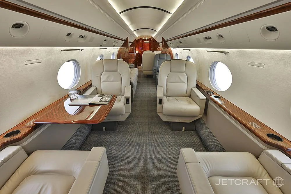 The luxurious cabin interior of a business jet features light leather seats and a polished wooden table.