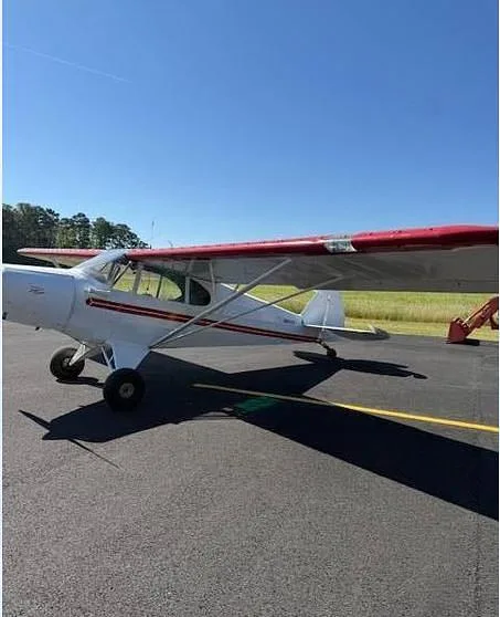 A side view of a white aircraft with red wings and stripes parked on an asphalt tarmac under a clear blue sky.