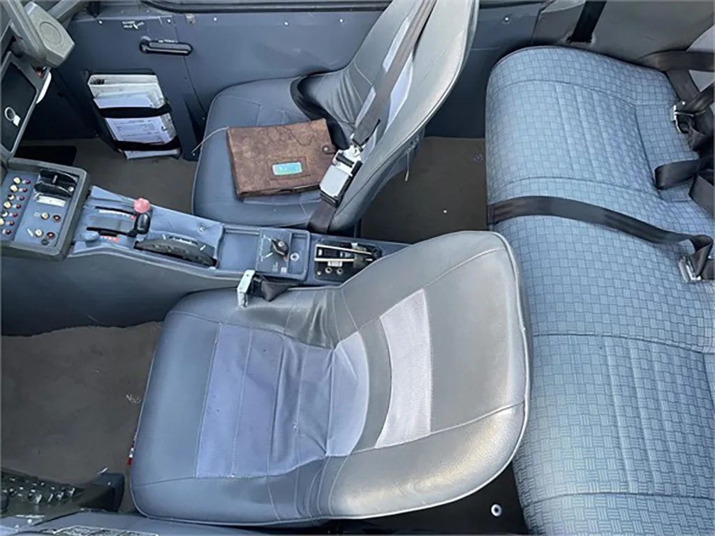 The interior cabin of a small aircraft, showing grey pilot seats and a patterned rear bench seat.