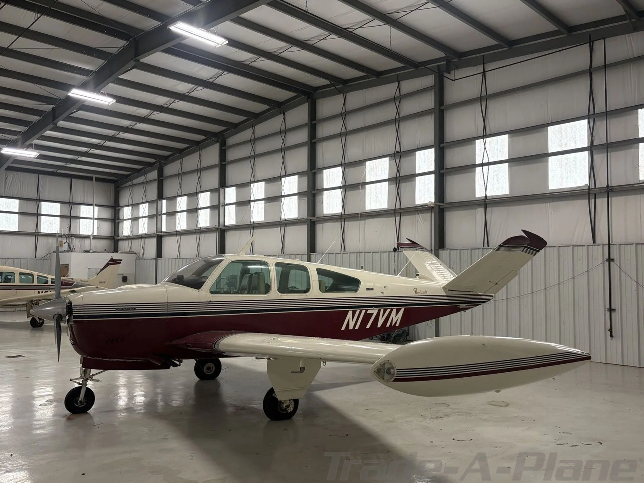 A white and maroon Beechcraft Bonanza N17VM parked inside a hangar, viewed from the front-right.