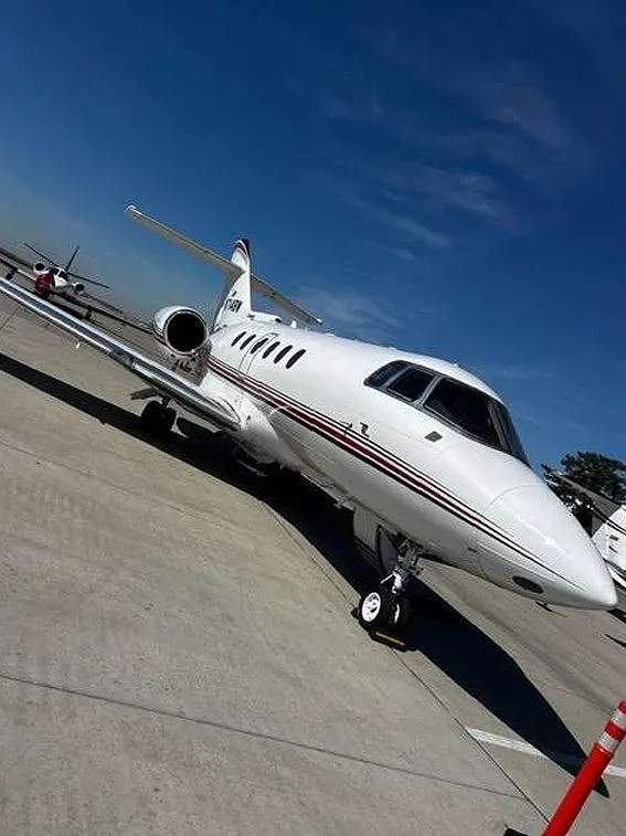 A white Hawker business jet with red and black stripes, tail number N714BW, parked on an airfield, viewed from a low angle.