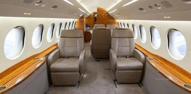 The luxurious interior of a private jet cabin with beige leather club seats and polished wood accents.