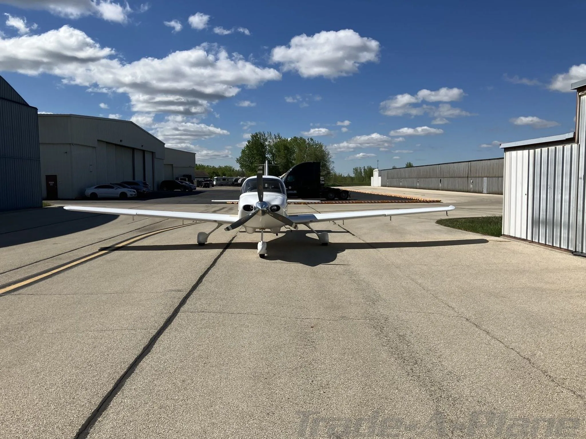 A white Cirrus SR20 aircraft, tail number N226CD, viewed from the front on an airfield tarmac with hangars in the background.