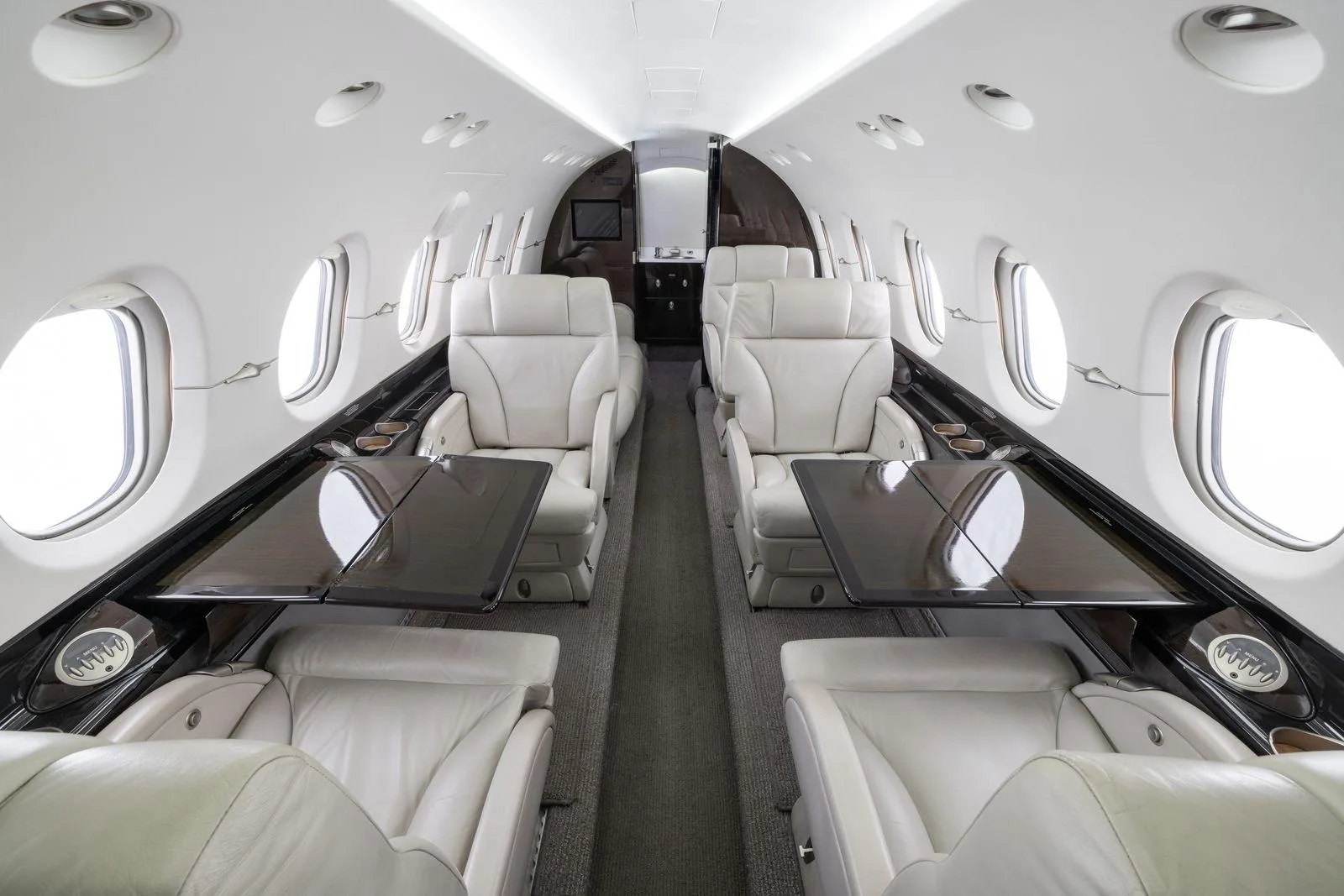 The aircraft's cabin interior with light-colored leather seats and dark fold-out tables.