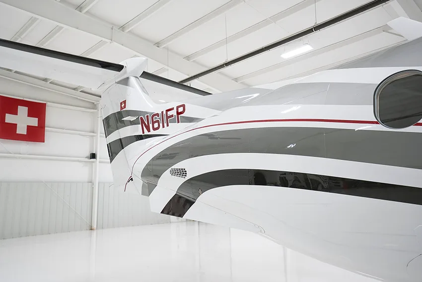 A close-up view of the tail section of a white Pilatus PC-12 aircraft with gray and red stripes, showing the registration N61FP.