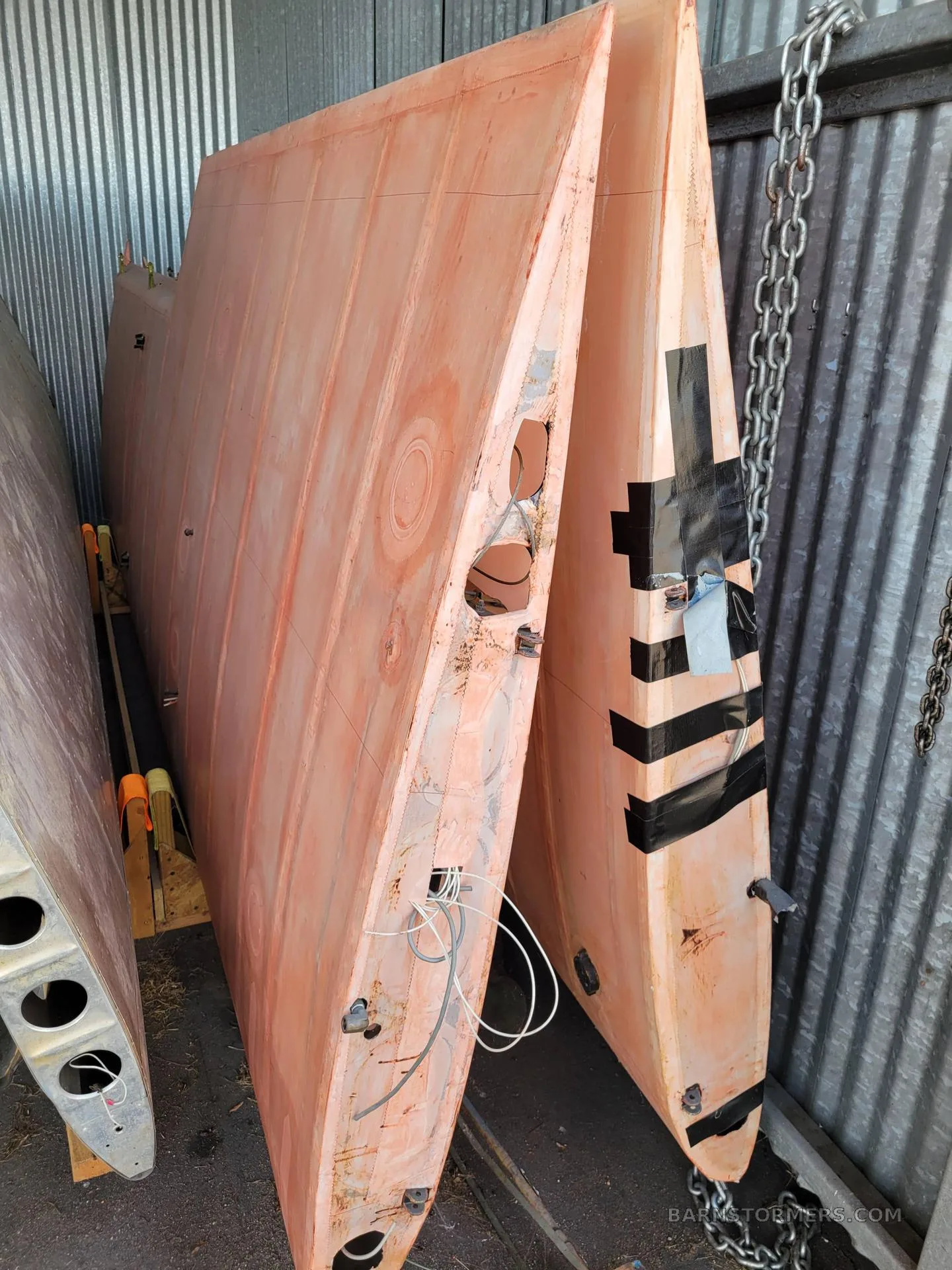 Two disassembled orange aircraft wing sections with exposed wiring, stored vertically in a hangar.