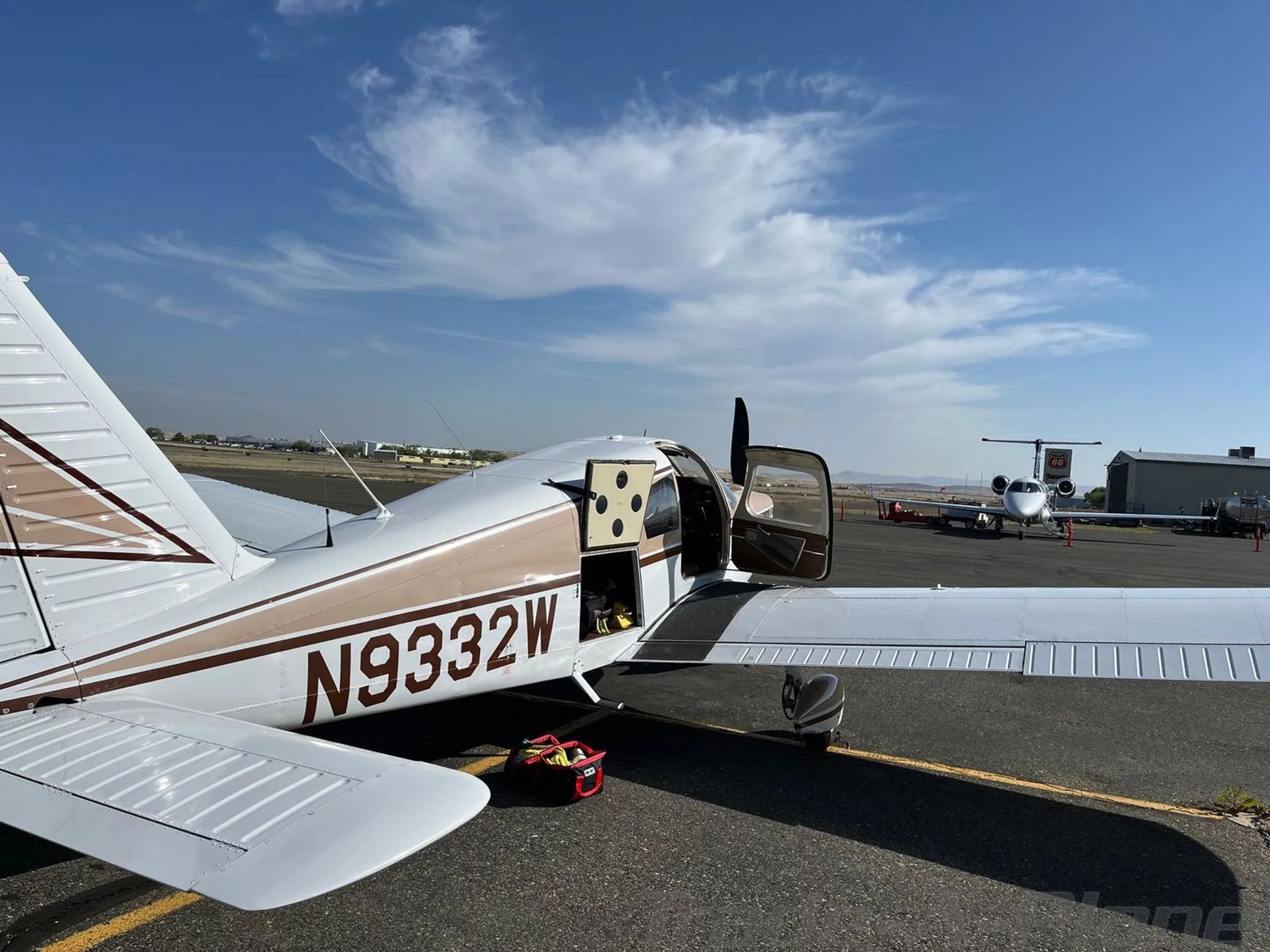 A Piper Cherokee 235, registration N9332W, with its door open, parked on an airfield next to other aircraft.