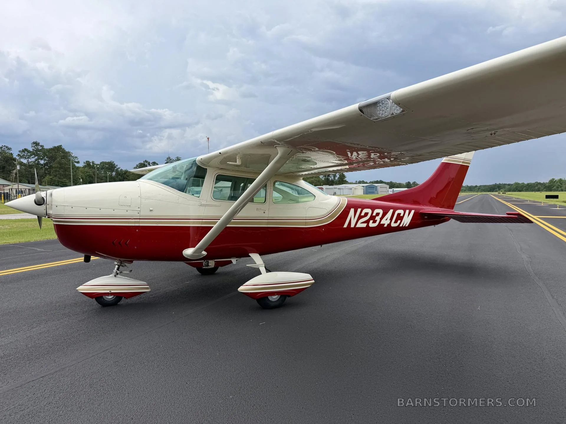 A three-quarter rear view of a red and white single-engine high-wing aircraft with registration N234CM parked on an airfield.