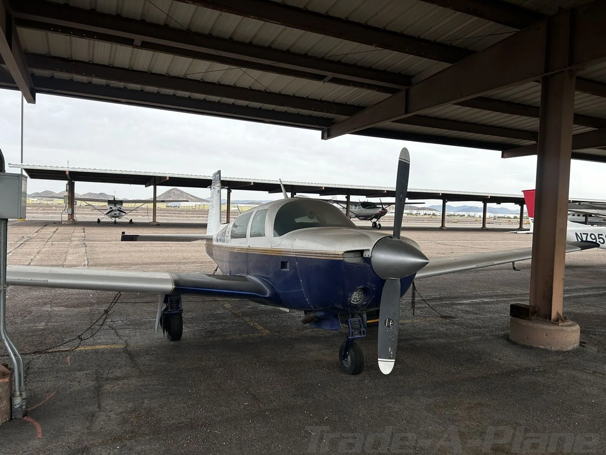 Front view of the blue and white single-engine aircraft N210RH parked under a covered shelter.