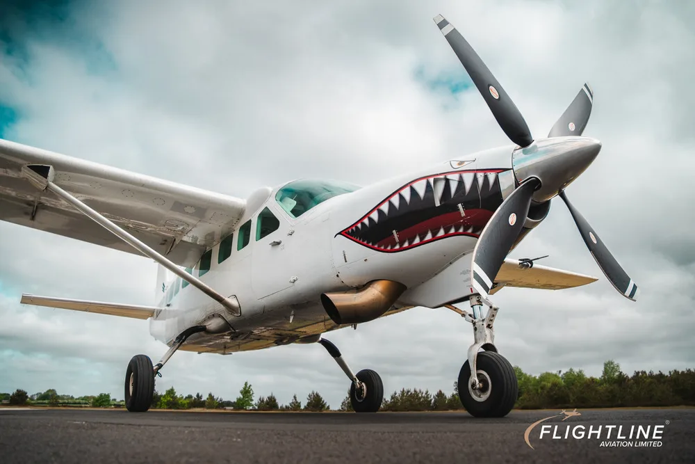 Low-angle front-side view of a white Cessna 208 Caravan with shark teeth nose art.