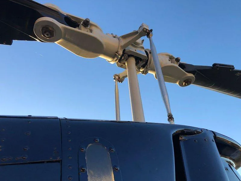 A detailed close-up of the main rotor hub and blades of a dark blue Bell 206 helicopter against a bright blue sky.