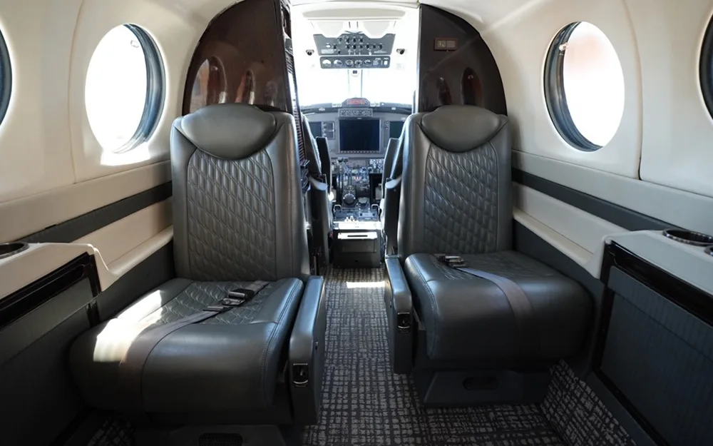 The aircraft cabin interior with two grey quilted leather seats facing forward, with a view into the cockpit.
