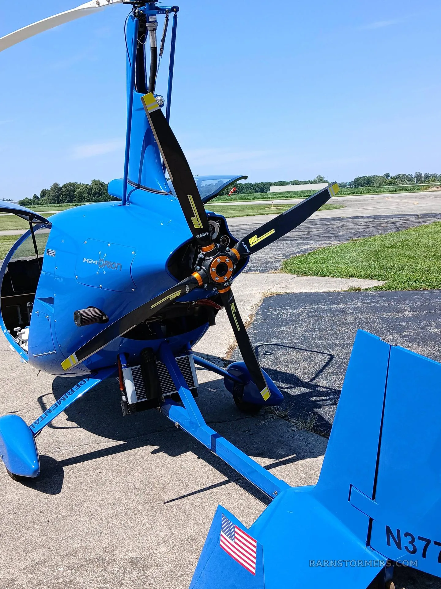 A close-up view of the blue M24 Orion gyrocopter's propeller and tail section with N3777W registration.