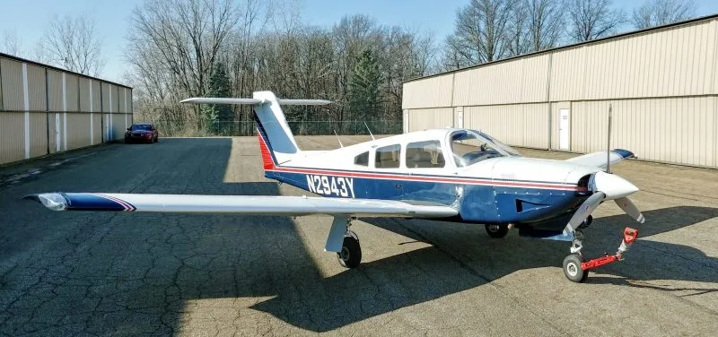 A blue and white Piper PA-28-140 Cherokee is parked on the tarmac.