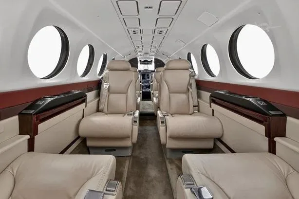 The aircraft's interior cabin features beige leather seats and dark wood trim, viewed from the rear.