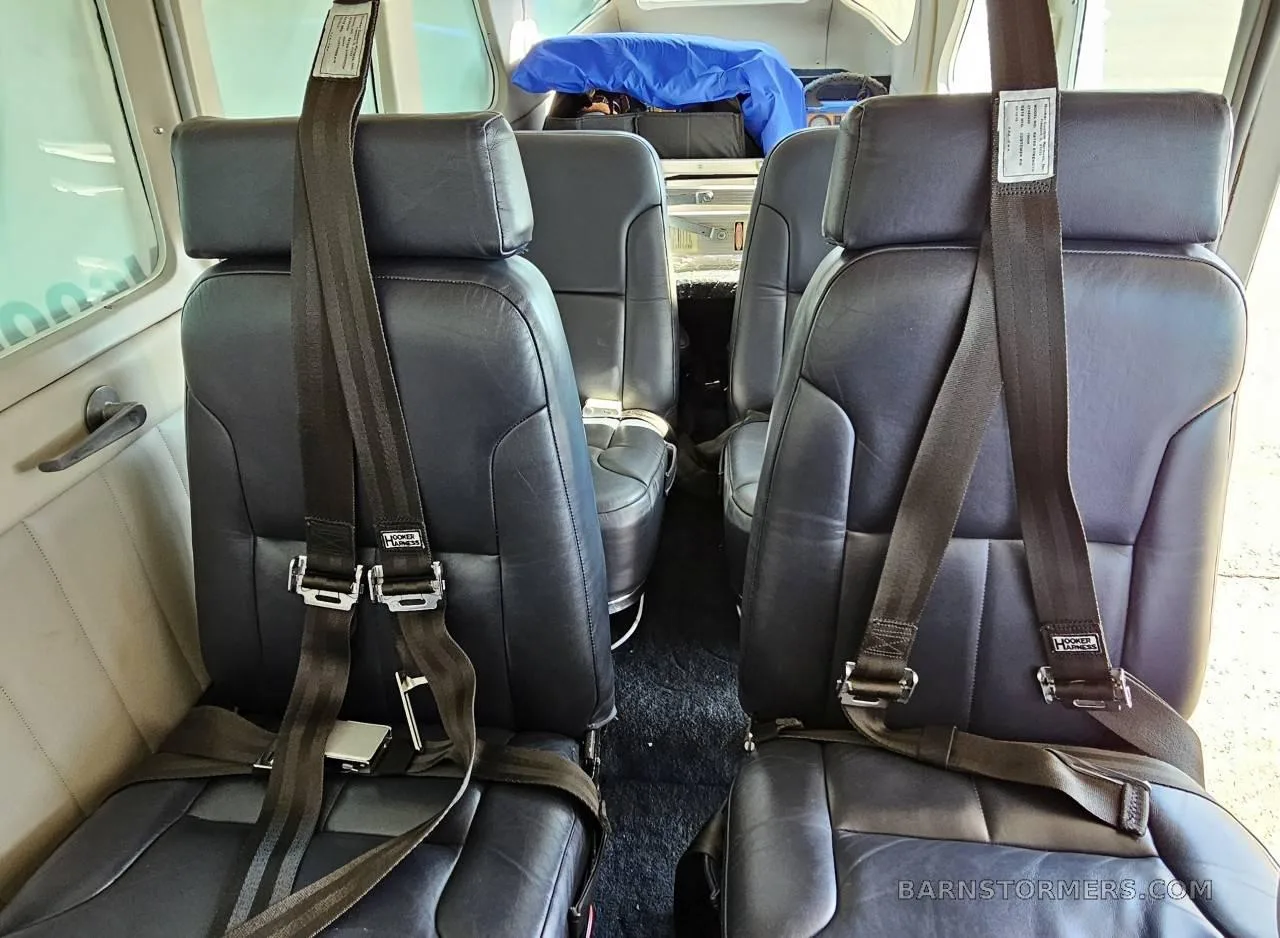 The interior cabin of an aircraft showing four black leather seats with seatbelts.