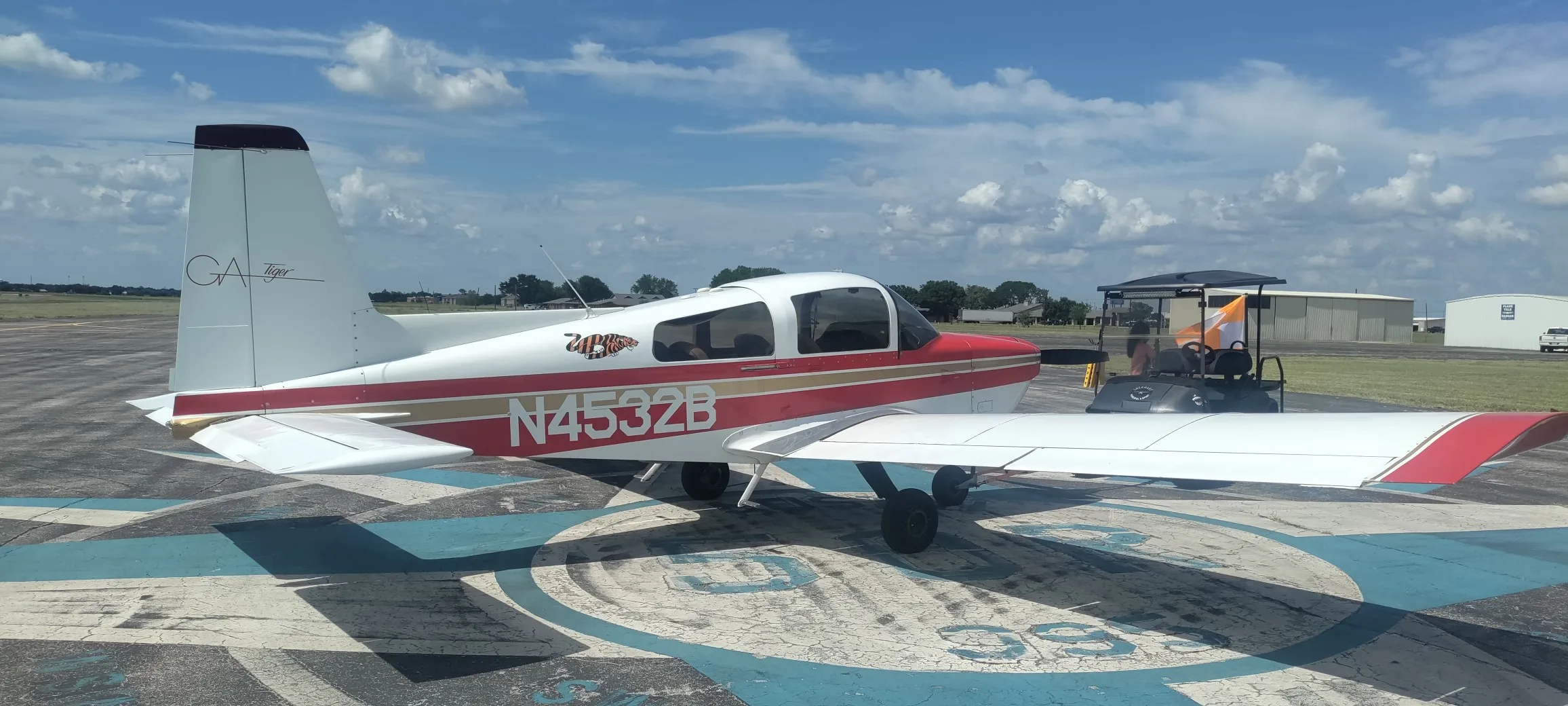 A red and white Gulfstream American GA-7 Cougar aircraft, N4532B, parked on an airfield next to a golf cart.