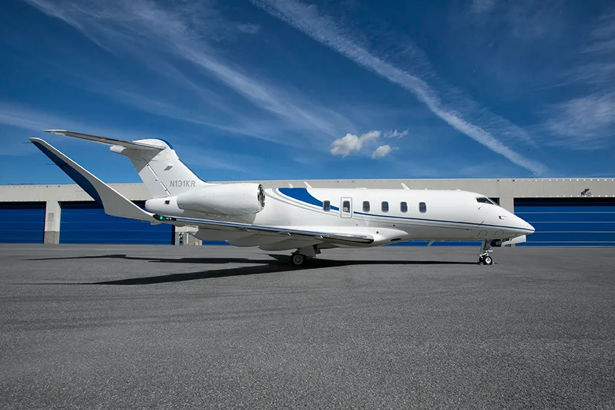 A white business jet with blue accents and registration N131KR is parked on an tarmac in front of blue hangar doors under a blue sky.