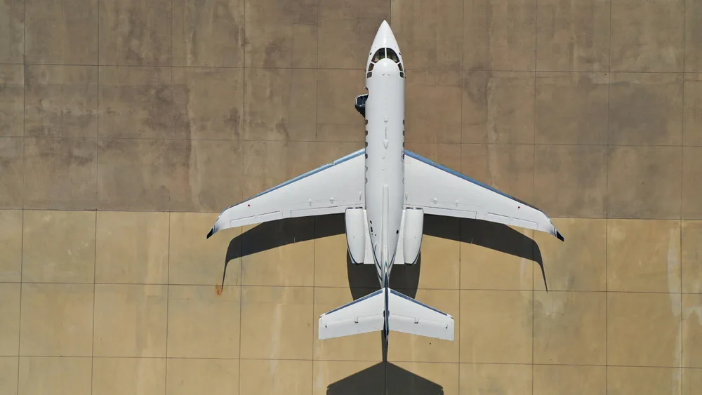 An overhead view of a white and blue Hawker 800XP business jet parked on a concrete tarmac.